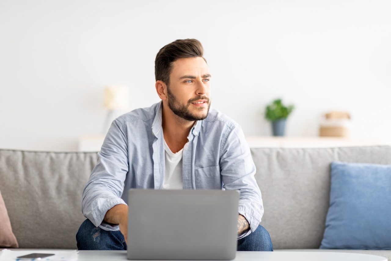 millennial freelancer working on laptop and looking aside thinking about successful business